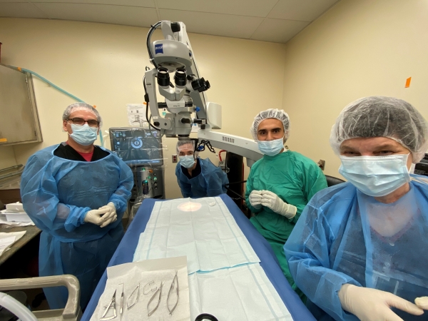 four people in surgery gear stand around a surgery table and look a the camera