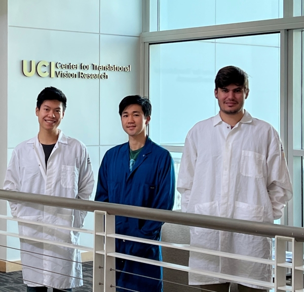 three men stand beside a railing with windows behind them